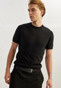 Sort kortærmet striktrøje med rund halsudskæring, lavet af blødt stof, parret med mørke bukser og et sort bælte med en sølvspænde.