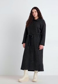 Dark gray knit dress with long sleeves, a collar, and a tie belt. Model wearing cream platform boots. Smooth texture, mid-calf length.