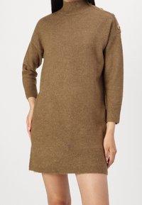 Abito maglione marrone con collo alto, maniche lunghe, polsini a costine e bottoni decorativi sulla spalla. Tessuto morbido.