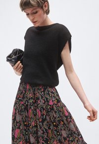 Czarny dzianinowy top z krótkimi rękawami w połączeniu z plisowaną spódnicą z kolorowymi kwiatowymi i paisley wzorami na czarnym tle.
