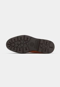 Suela de goma marrón con un patrón de relieve texturizado que presenta flechas y símbolos, diseñado para la tracción y la durabilidad.