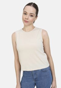 Top sin mangas beige hecho de una tela suave y elástica; escote redondo; diseño ajustado, combinado con jeans azul de cintura alta.