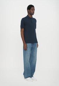 Marineblå polo skjorte laget av bomull, med klassisk krage og korte ermer, kombinert med lyseblå, komfortable denimbukser og hvite joggesko.