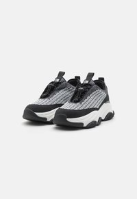 Černobílé tenisky s texturovaným svrškem segeometrickými vzory, zaoblenou špičkou, silnou bílou podrážkou a elastickým šněrovacím systémem.