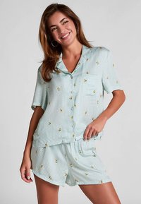 Lichtblauw geruit pyjama set met korte mouwen en bloemenprint. Het bovenstuk heeft een knoopsluiting en een opgestikt zakje; de korte broek heeft een elastische tailleband.