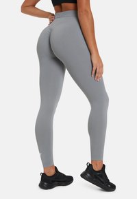 Grijze leggings met een gladde textuur, hoge taille en naaddetails, gedragen met zwarte sportschoenen.