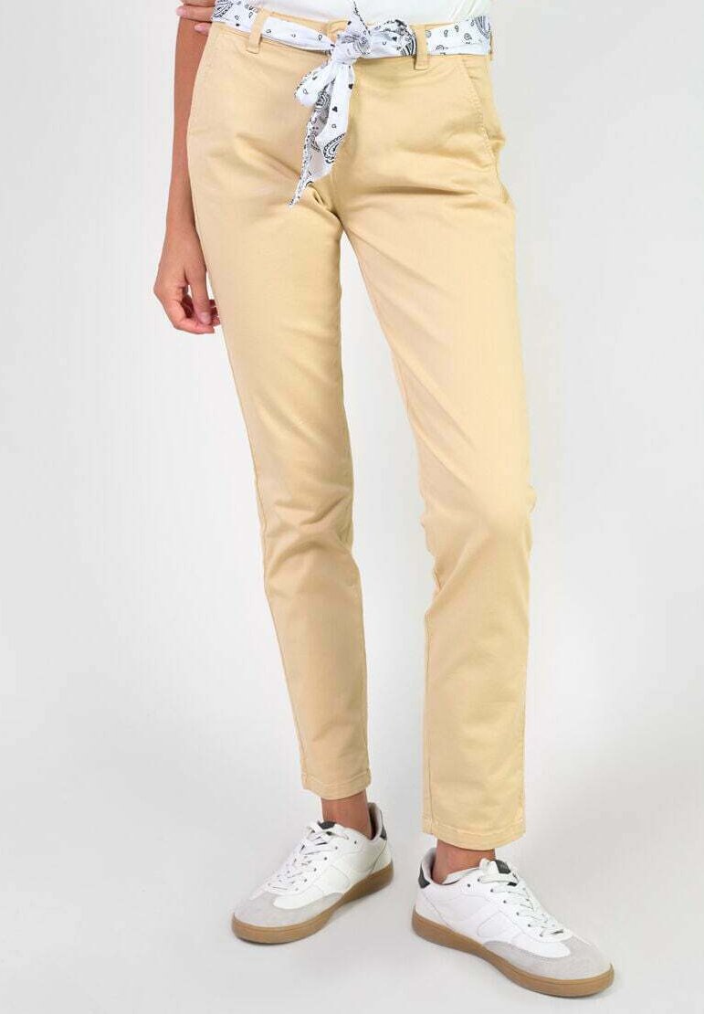 Chinos beige à coupe slim, avec des poches avant et une ceinture de tissu blanche, associés à des baskets blanches et grises.