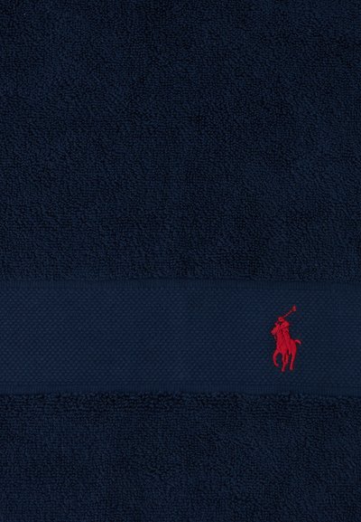 Υφασμα με υφή σε ναυτικό μπλε, με οριζόντια ζώνη που φέρει μικρή κόκκινη κεντημένη φιγούρα παίκτη πόλο πάνω σε άλογο.