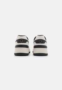 Sorte og hvide sneakers med en overdel i læder, polstret krave, en struktureret hæl og en tyk hvid mellemsål med en sort ydersål.