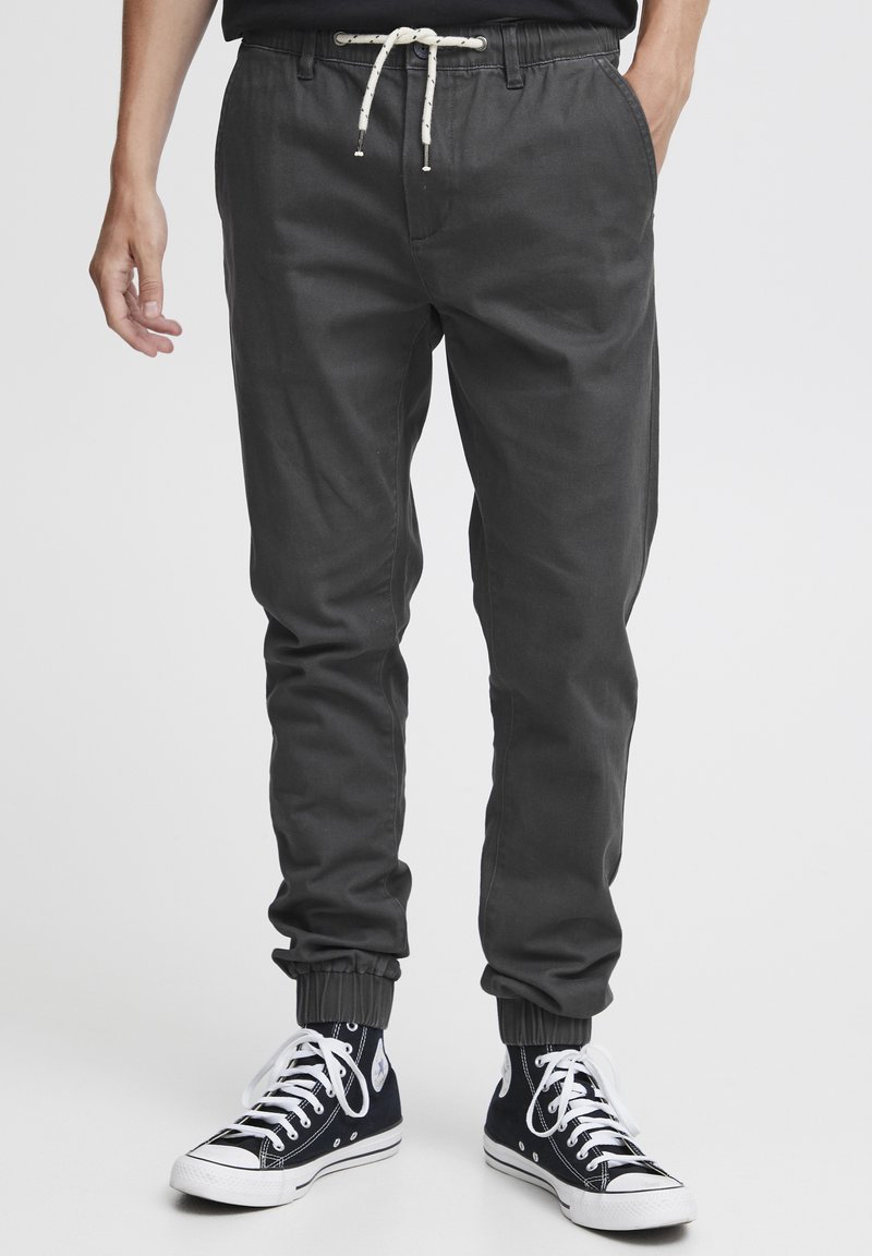Mørk grå joggebukser med elastisk midjebånd, justerbar snor, ribbede mansjetter og sidelommer. Brukt med svarte høye sneakers.