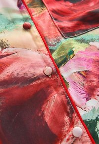Kleurrijke stoffen met een bloemenpatroon in rood, roze en groene tinten, met een gestructureerd oppervlak en een lichtkleurige knoopdetail.