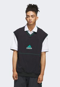 Top sans manches noir avec un décolleté en V et des accents verts, arborant le logo Adidas en turquoise. Fabriqué en matériau léger avec une coupe décontractée.