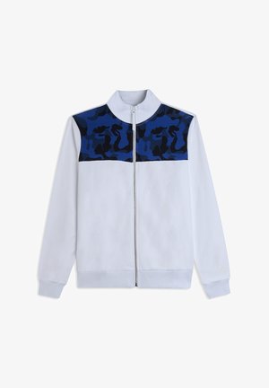 Chaqueta blanca con cremallera, con un patrón de camuflaje en azul y negro en los hombros y la parte superior del pecho, que cuenta con mangas largas y un cuello alto.