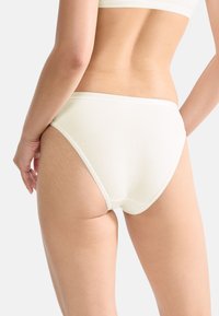 Helle, cremefarbene Baumwollslips mit glatter Textur, hohem Schnitt und kontrastierendem elastischem Bund. Verfügt über minimale Nähte und nahtlose Seiten.