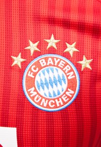 Κόκκινο ύφασμα με το λογότυπο του συλλόγου FC Bayern München και πέντε χρυσά αστέρια κεντημένα από πάνω.