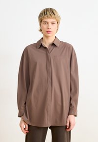 Camicia button-up marrone realizzata in tessuto leggero con una vestibilità rilassata, dotata di taschino sul petto, colletto e maniche lunghe con polsini.