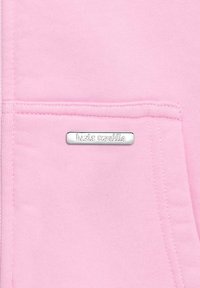 Light pink sweatshirt fabric with a front pocket, featuring a silver rectangular tag with the text "basics republiq." Soft texture, simple design.