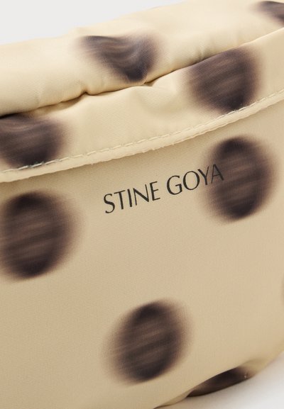 Tissu matelassé beige avec de grands pois bruns foncés flous et le nom de la marque Stine Goya imprimé en noir.
