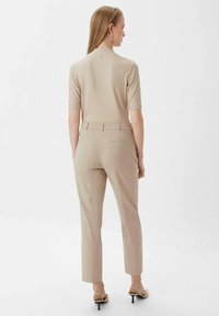 Jasno beżowy, prążkowany top z krótkim rękawem, w połączeniu z jasnobeżowymi spodniami o kroju dopasowanym. Slim fit, z wykończeniem z tyłu i kieszeniami. Czarne, wyższe klapki.