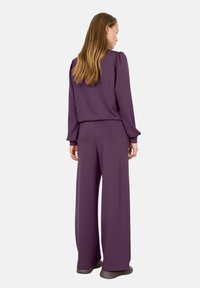 Conjunto de lounge morado que incluye una blusa de manga larga con hombros abullonados y pantalones de pierna ancha. Tejido suave con textura lisa, diseñado para la comodidad.