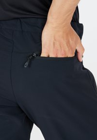 Svarta träningsbyxor med mjuk textur och elastisk midjeband, med en dragkedjeförsedd sidoficka på vänster höft.