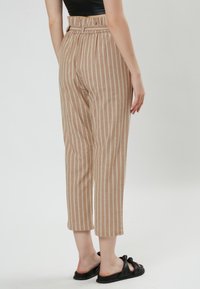 Pantalones de rayas beige con una cintura alta, trabillas, y un corte cropped, que presentan una tela texturizada y un corte recto. Sandalias negras visibles.