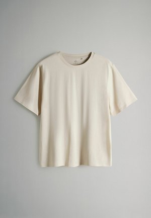 Trumpomis rankovėmis marškinėliai šviesiai smėlio spalvos, pagaminti iš minkšto medvilnės audinio. Turi apvalų iškirpimą ir laisvesnį siluetą, be jokių raštų ar papuošimų.