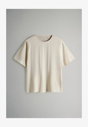 Koszulka z krótkim rękawem w jasnobeżowym kolorze, wykonana z miękkiej bawełny. Posiada okrągły dekolt oraz luźny krój, bez wzorów i zdobień.