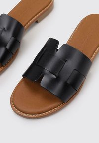 Sandales à glissière en cuir noir avec une large sangle texturée présentant un design découpé géométrique, sur un semelle rembourrée couleur tan.