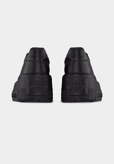 Paire de baskets plateformes noires vues de dos, avec des motifs embossés sur des semelles épaisses et texturées et des tiges en cuir lisse.