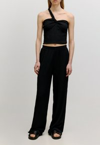Zwarte two-piece outfit met een een-schouder crop top met een geknoopt detail en losse, hoge taille broeken met een textuurafwerking.