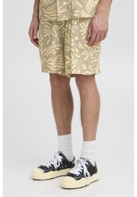 Beežid lühikesed püksid lehendimustriga, valmistatud kergest kangast, kantud mustade lõuatsikute ja valgete sokkidega. Igapäevane, lõdvestunud istuvus.