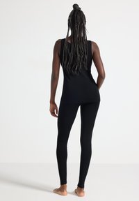 Svart ärmlös topp och matchande leggings, båda i stretchigt tyg, med en åtsittande design, slät textur, utan synliga mönster eller hårdvara.