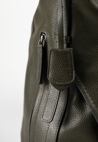 Borsa in pelle verde scuro con texture, dotata di zip visibile e nome del marchio "aunts & uncles" impresso su un’etichetta in pelle attaccata.