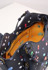 Mustaharja nahkakäekott, millel on värvikas värvi pritsimise disain, oranž sisemus ja messingust riistvara, kahe tõmblukuga koti osaga.