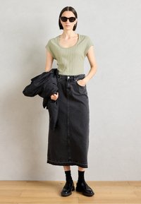 Vaaleanvihreä ribbipintainen lyhythihainen toppi, musta farkkupitkä hame, musta kuvioitu takki, mustat loafersit ja aurinkolasit neutraalilla taustalla.