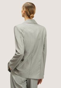 Blazer su misura grigio chiaro caratterizzato da un design strutturato, sottili righe verticali, colletto a scollatura e una texture liscia con una vestibilità rilassata.