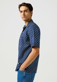 Camisa de botones de manga corta en color navy con estampado floral blanco, con cuello y corte relajado. Fabricada en tejido ligero.