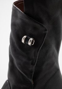 Nära bild av svart läderstövel med mjuka veck och en detalj i silvermetall på ovansidan.