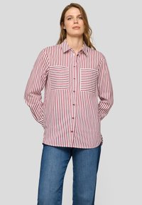 Red and white striped button-up shirt with two horizontal stripe pockets, collared neckline, and long sleeves. Worn with blue jeans.