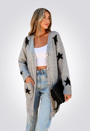 Cardigan gris de punto con patrones de estrellas negras, botones frontales y bolsillos laterales. Combinado con jeans de mezclilla azul claro y un bolso negro.