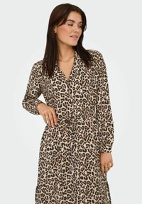 Leopard mönstrad klänning med krage, långa ärmar och bälte i midjan, tillverkad av ett lätt texturerat tyg. Basfärg i neutrala toner.