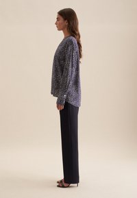 Blusa blu navy con motivo a pois bianchi, vestibilità ampia, maniche lunghe, indossata con pantaloni neri a gamba dritta e sandali neri con tacco.