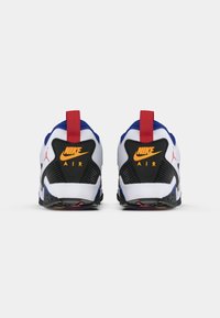 Un paio di scarpe Nike Air bianche, blu, nere e rosse viste da dietro, con loghi Nike arancioni e linguette rosse sul tallone.