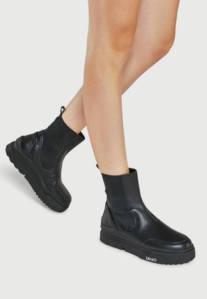 Bottes noires à cheville en cuir lisse et tissu élastique, dotées d'une semelle en caoutchouc épaisse et d'une tirette à l'arrière pour faciliter l'enfilage.