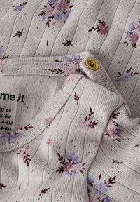 Jasnoszara tkanina z pionowymi paskami, zdobiona kwiatowym wzorem w różowym i fioletowym kolorze. Zawiera prążkowany dekolt oraz złote guziki jako detal.