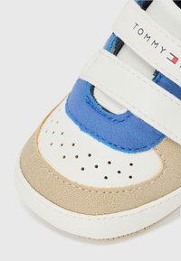 Sneaker per bambino con pannelli blu, bianchi e beige. Caratterizzato da strappi in Velcro, perforazioni sulla punta e materiali testurizzati. Logo del marchio visibile.