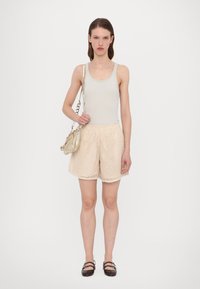 Lichtgrijs tanktop en beige gestructureerde shorts met een koordtaille, gecombineerd met een kleine lichte handtas en donkere platte schoenen.