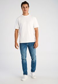 Biała koszulka z krótkim rękawem, proste niebieskie dżinsy denimowe oraz białe trampki. Prosty design, gładka tekstura i luźny krój.