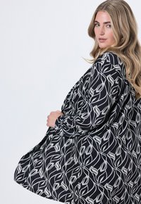 Černá blůza s bílým květinovým vzorem, dlouhými rukávy a volným střihem. Tkanina vypadá hladce s mírným leskem.